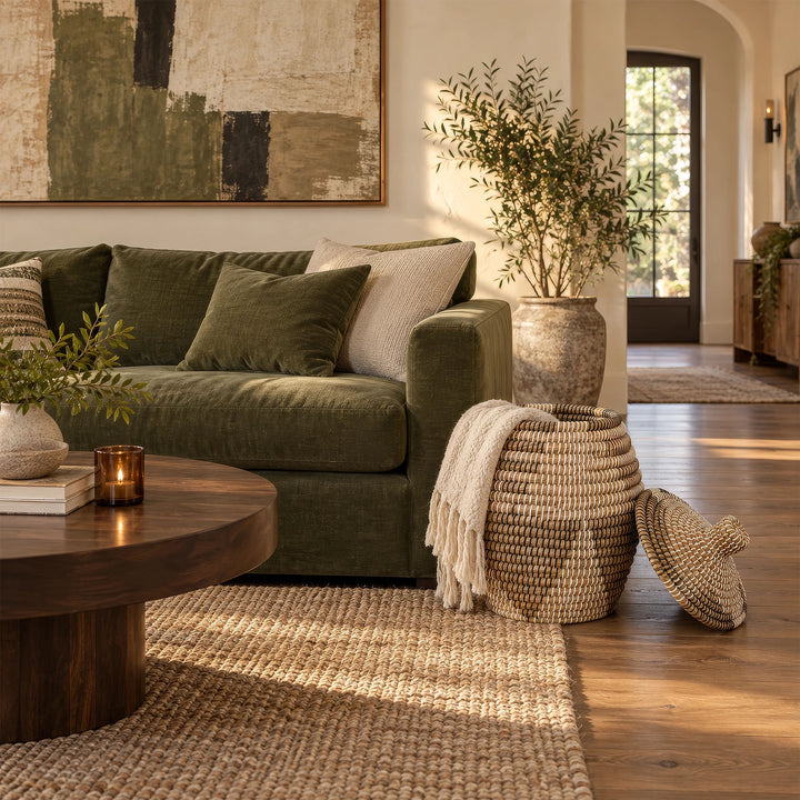 An open seagrass basket in natural/brown/black/white with a capacity of about 30 liters and a light-colored cover, placed next to the sofa.