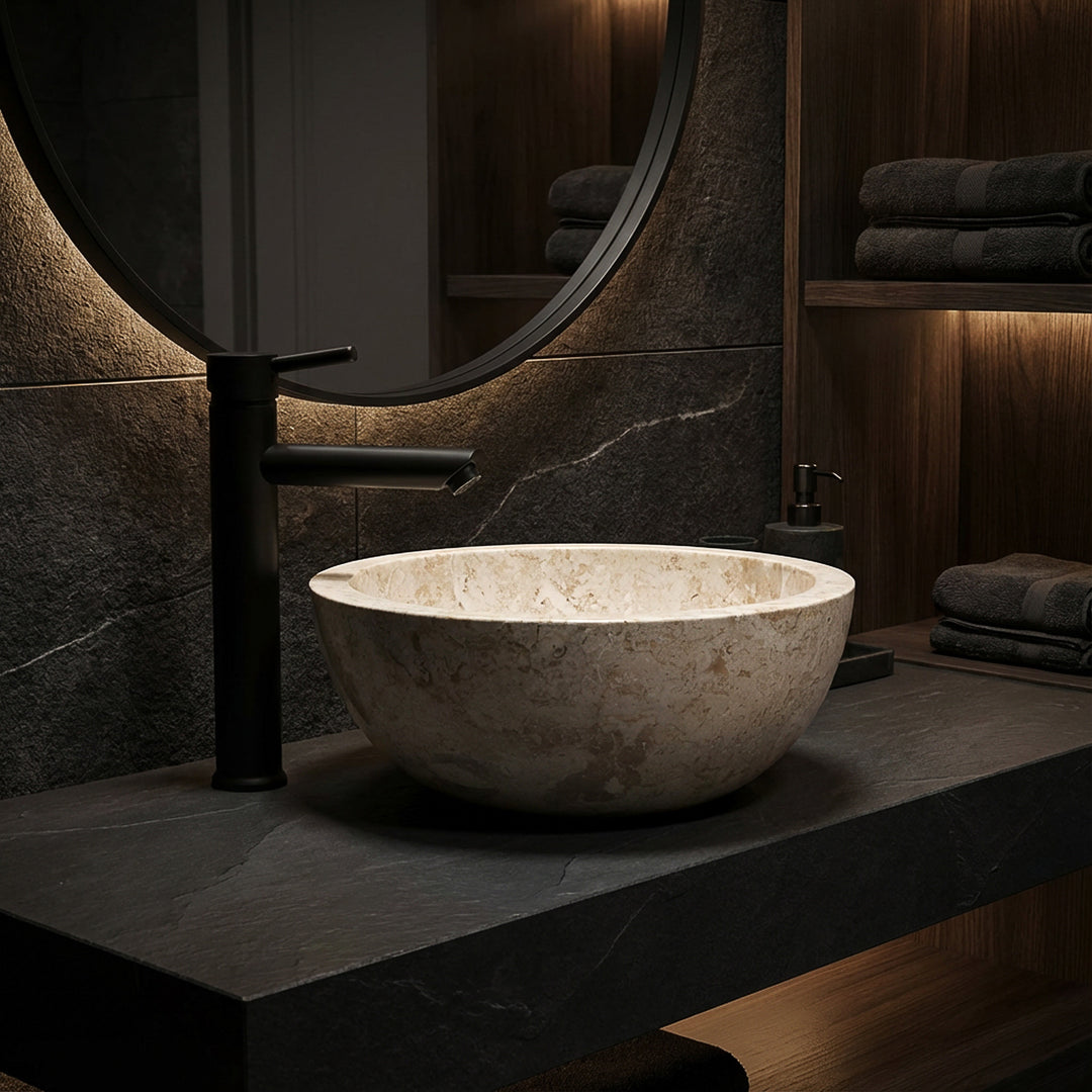 Round countertop basin made of light marble on a dark stone slab with a black fitting in an elegant bathroom ambience