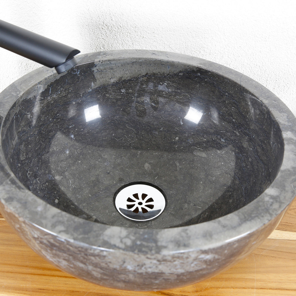 Detailed view of a round stone basin with a polished inner surface and a central drain on a wooden plate