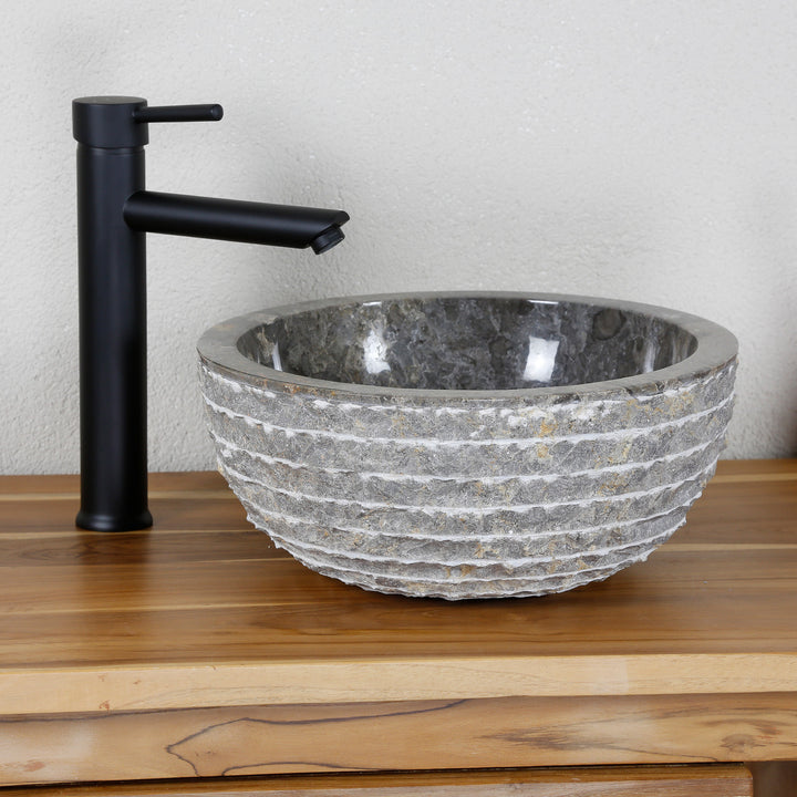 Round countertop basin made of natural stone with a structured surface on a wooden top, combined with a black stand-alone tap