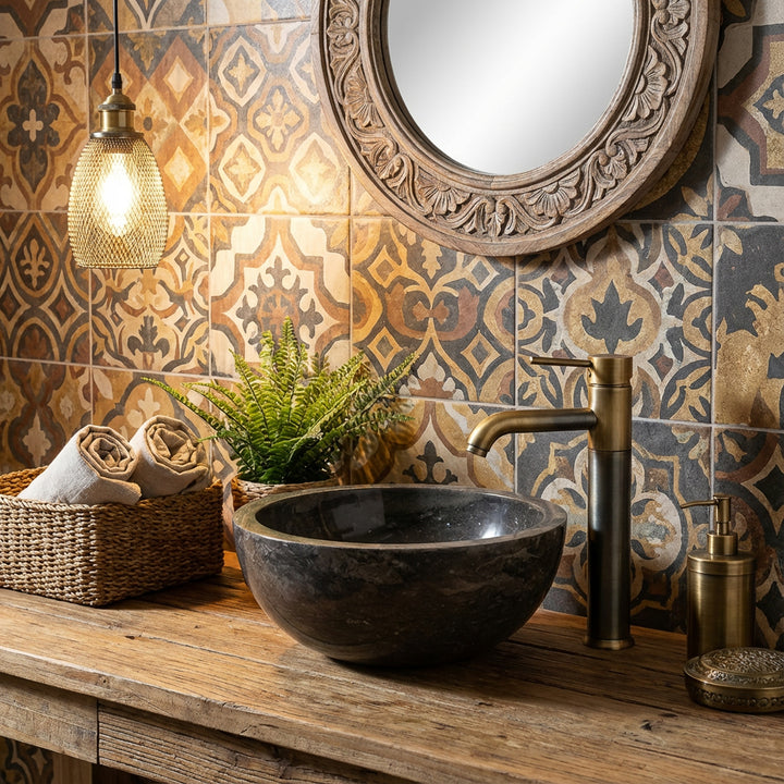 Round countertop basin made of stone on a wooden washbasin with a brass fitting in front of patterned tiles in a warm bathroom ambience