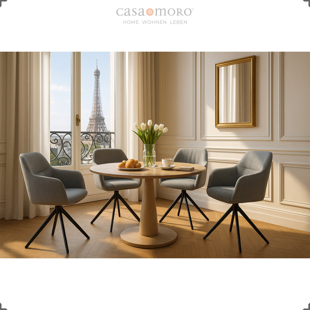 Four 360° swivel upholstered chairs with gray armrests around a round wooden table in an elegant dining room with a view of the Eiffel Tower