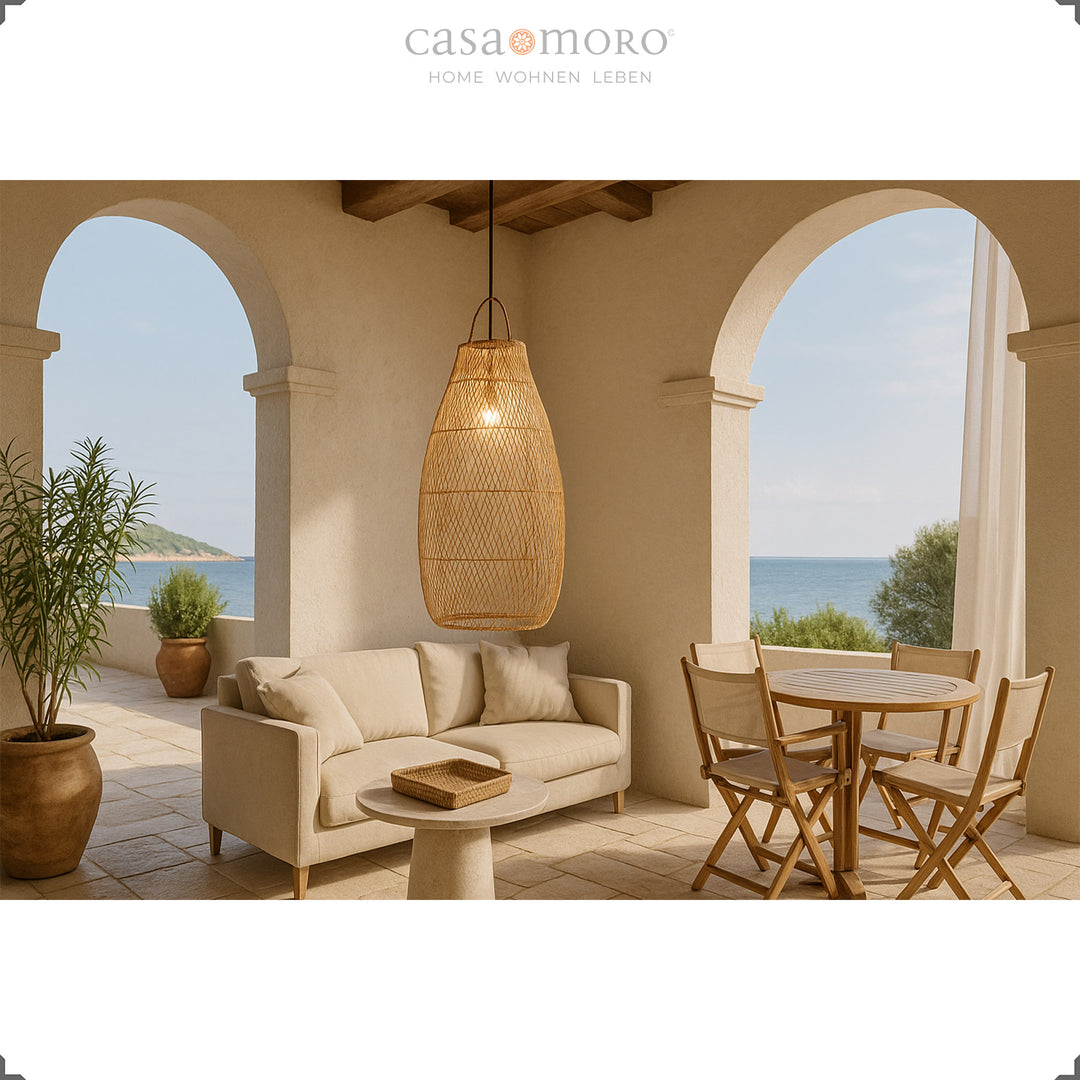 Tall rattan lamp on Mediterranean terrace above dining table and sofa with sea view