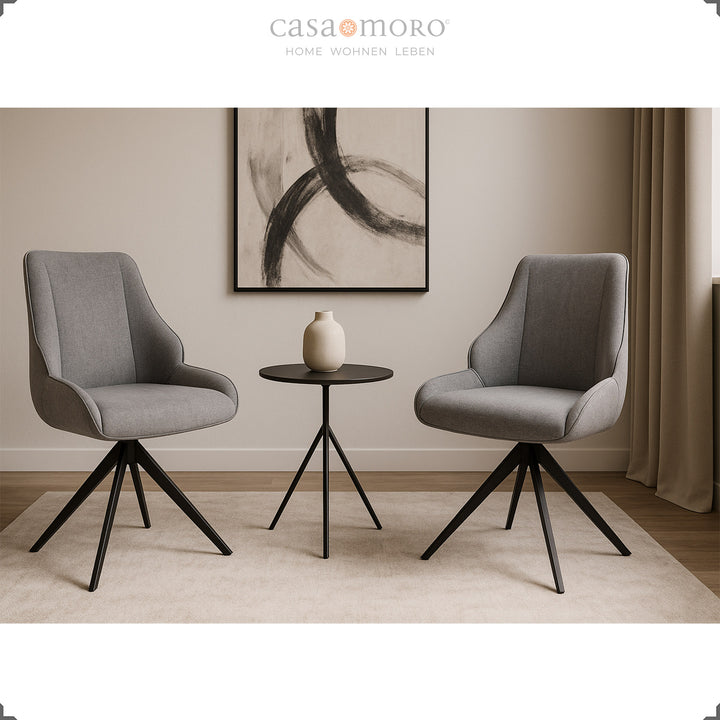 Two 360° rotating dining chairs in gray with a black metal frame next to a round side table in a modern, brightly furnished living room