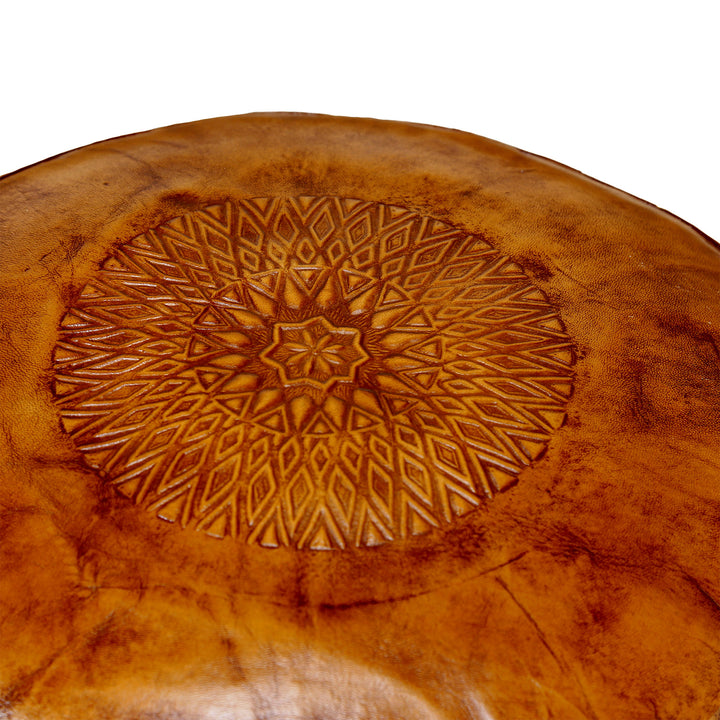 Detailed view of the embossed top of a leather pouf in warm brown with a fine oriental pattern and natural leather structure.