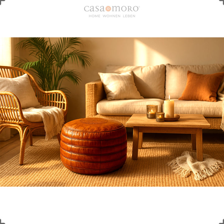 Living scene in boho style with a round leather pouf in warm brown in front of a sofa and rattan armchair, surrounded by candlelight and natural materials – a harmonious ambience.