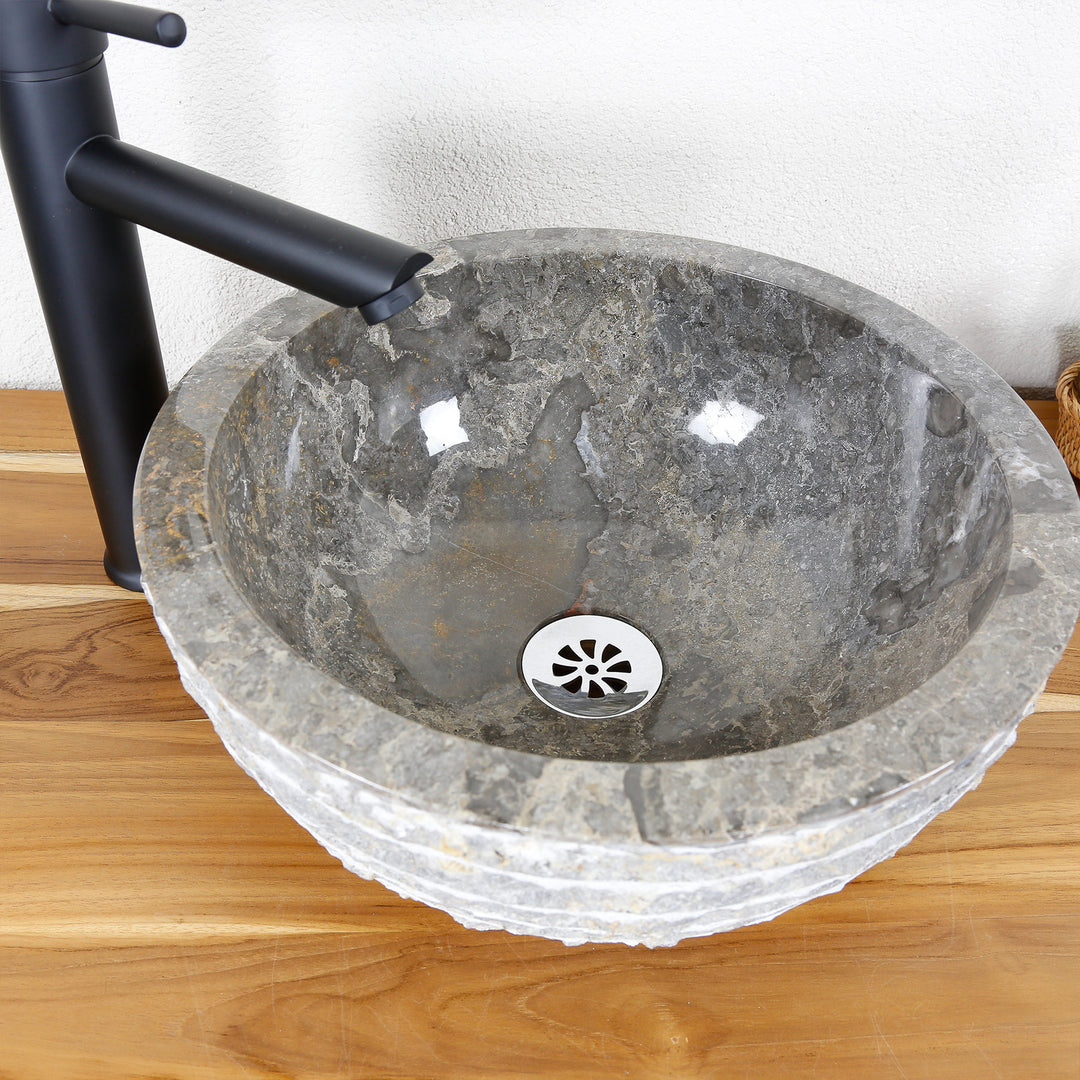 Round countertop washbasin made of natural stone with a polished inner surface and a structured outer edge on a wooden top