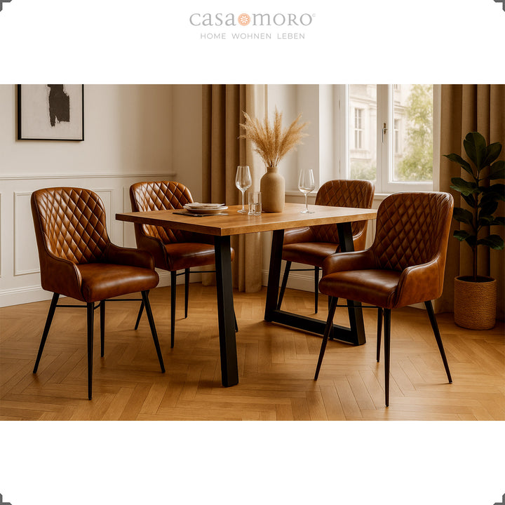 Four antique brown leather chairs with diamond quilting at a wooden table in an elegant dining room with parquet floors, light wall paneling and natural decorations.