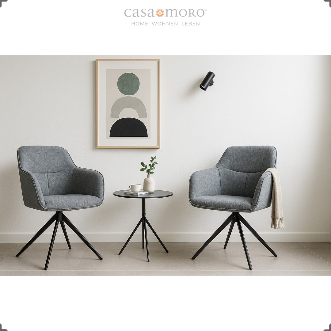 Two 360° rotating upholstered chairs with armrests in gray next to a round side table in a modern living room with bright wall decoration