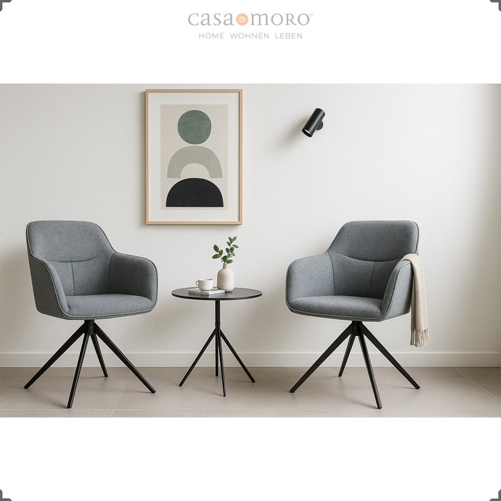 Two 360° rotating upholstered chairs with armrests in gray next to a round side table in a modern living room with bright wall decoration