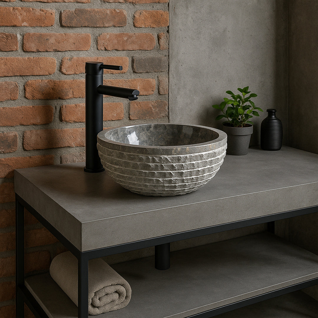 Gray stone washbasin as a countertop washbasin on a concrete vanity unit, modern bathroom with brick wall and black fittings
