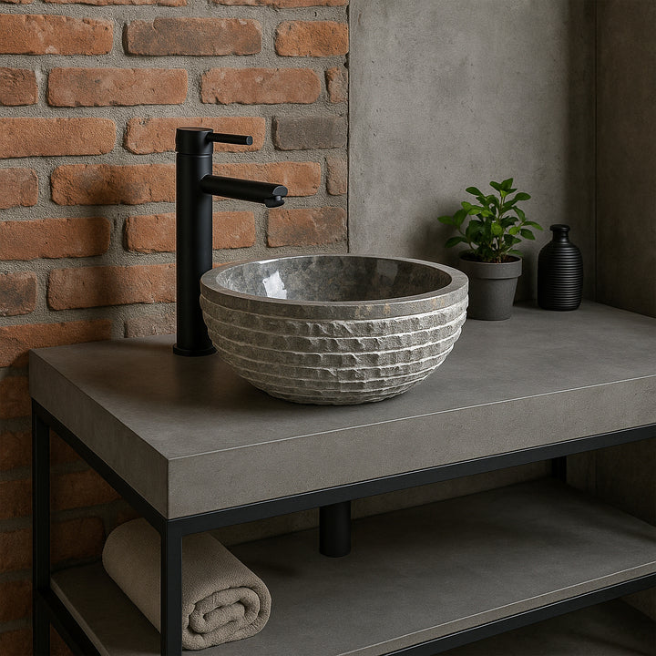 Gray stone washbasin as a countertop washbasin on a concrete vanity unit, modern bathroom with brick wall and black fittings