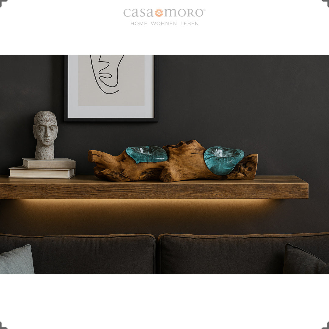 Elongated tea light holder made of glass and burl wood on a wall shelf, its warm light complements the stylishly dark living room ambience.