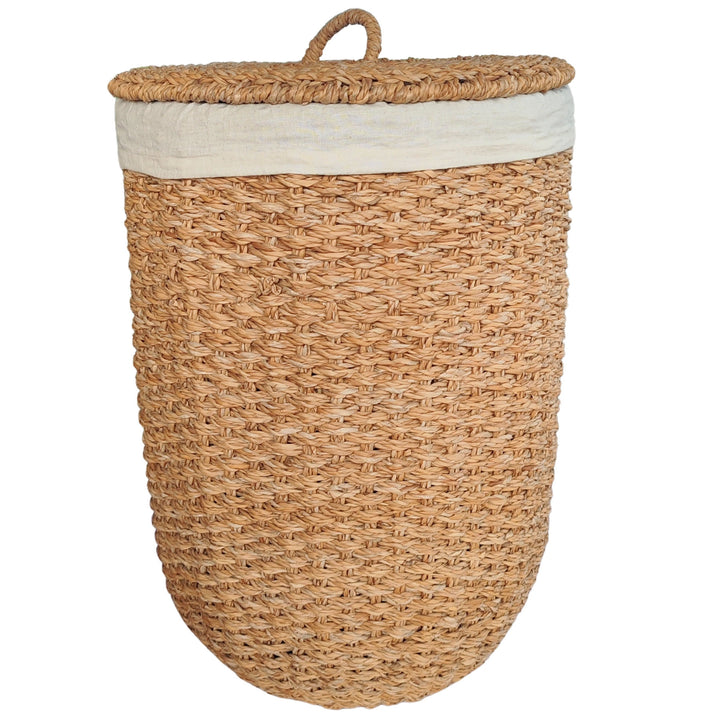 An open laundry basket made of natural-colored seagrass with a light-colored fabric insert and a lid that rests against the side.