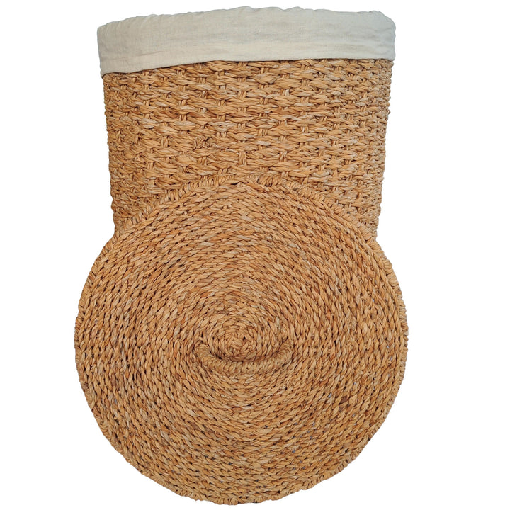 Laundry basket made of natural-colored seagrass with a light-colored fabric insert and a lid placed in front of it.