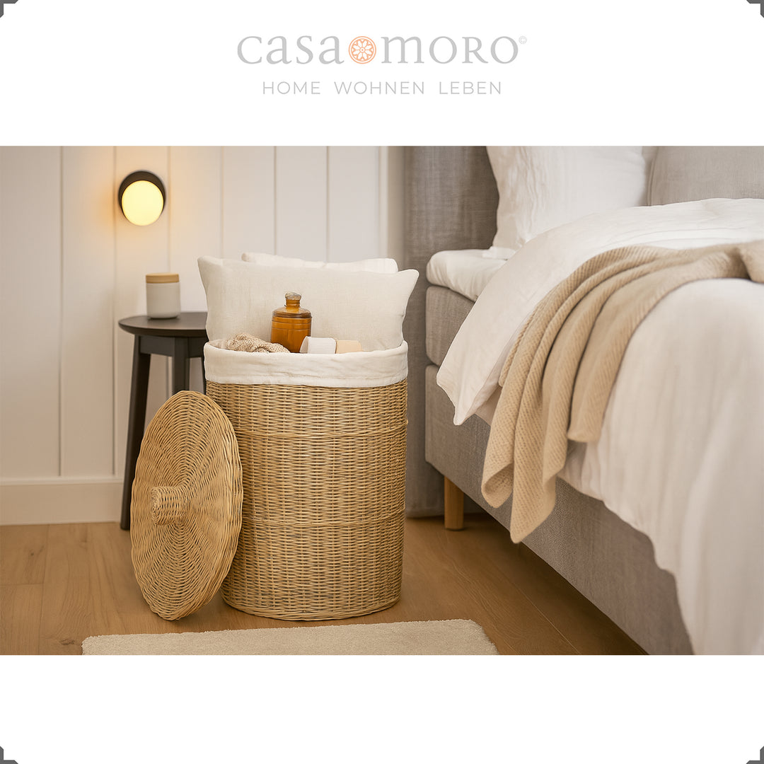Round rattan laundry basket with lid in the bedroom, filled with pillows, blankets and toiletries