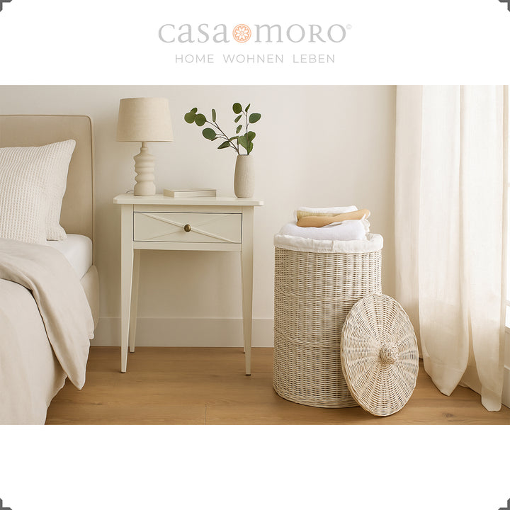 Bright white wash laundry basket in the bedroom, combined with warm natural tones, curtains and bedside table