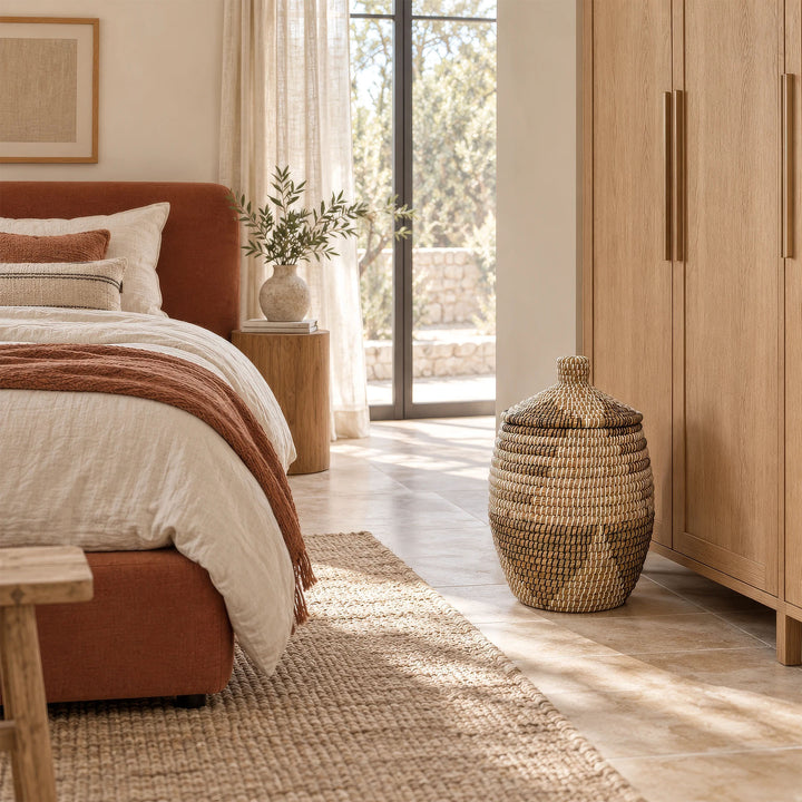 A seagrass laundry basket in natural/brown/black/white with a lid and a capacity of approximately 30 liters in the bedroom.